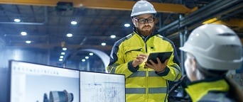 engineer in hardhat with iPad meeting with engineer at desktop